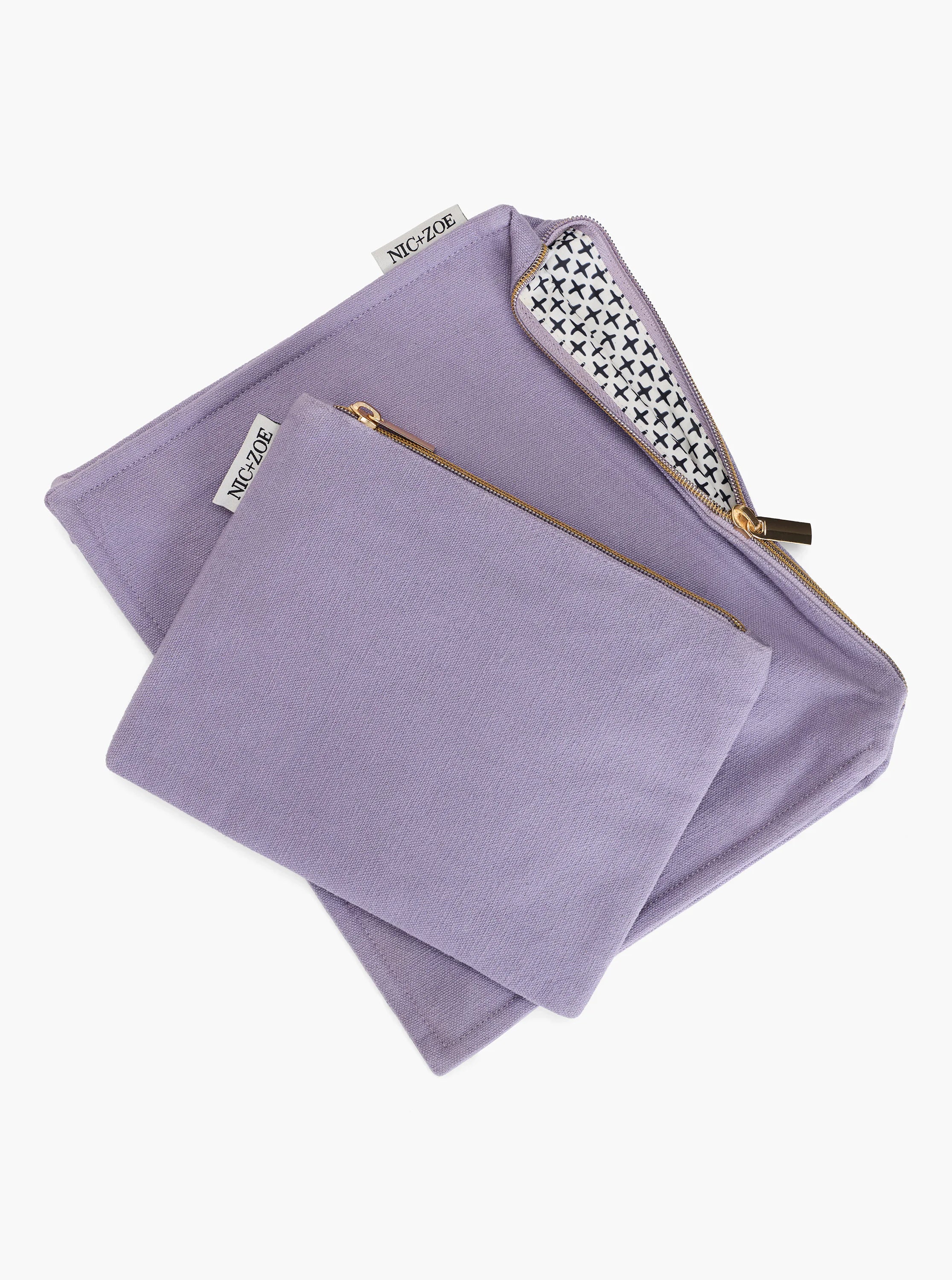 Two lavender pouches, one larger, one smaller, with gold zippers. The larger pouch reveals a white lining with a black...
