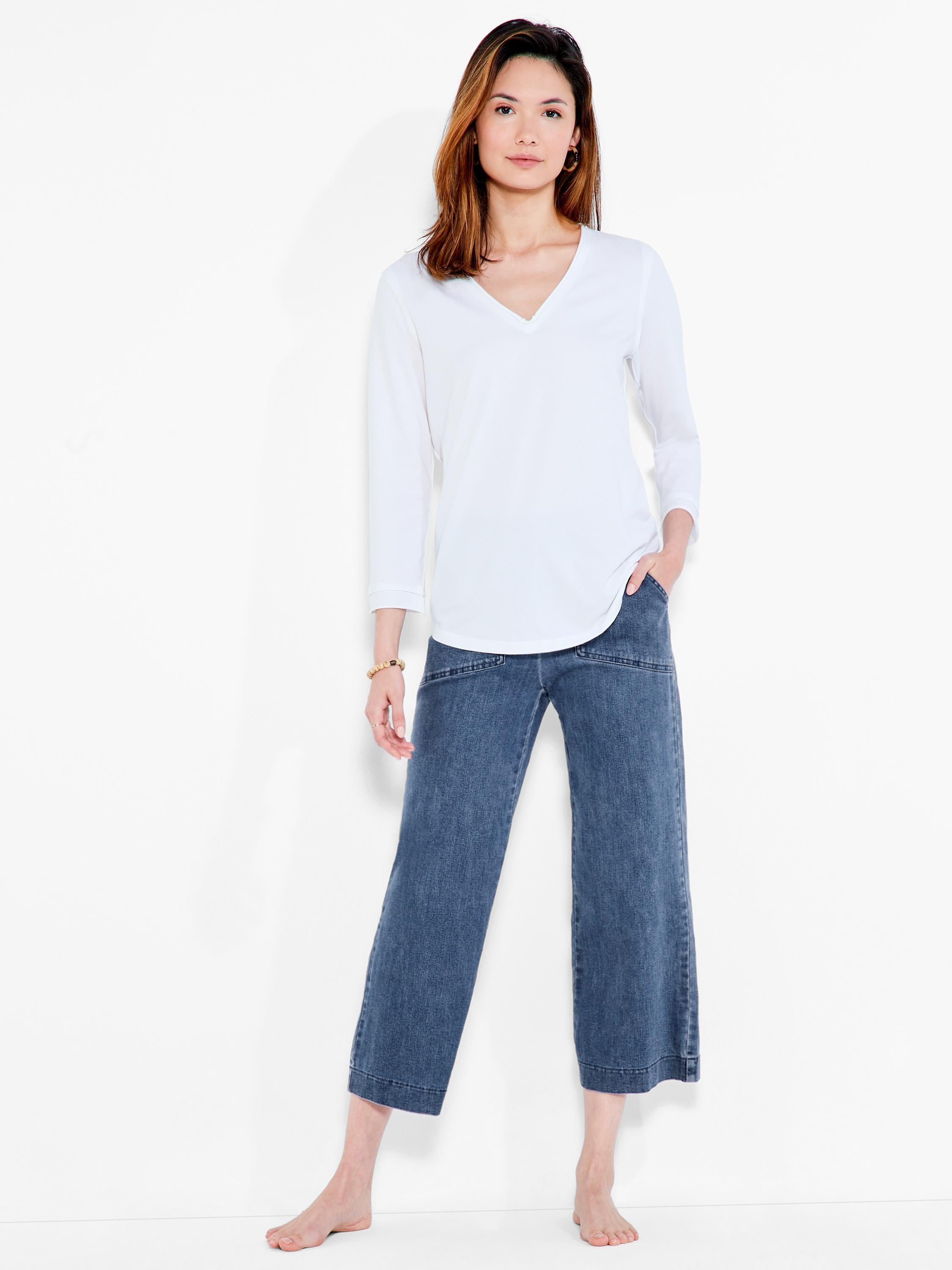The model wears a white, relaxed fit, 3/4 sleeve v-neck top tucked into wide-leg denim pants.