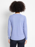 Back view of a periwinkle long-sleeve top. White inner layer visible at neck, rounded hem. Relaxed fit.