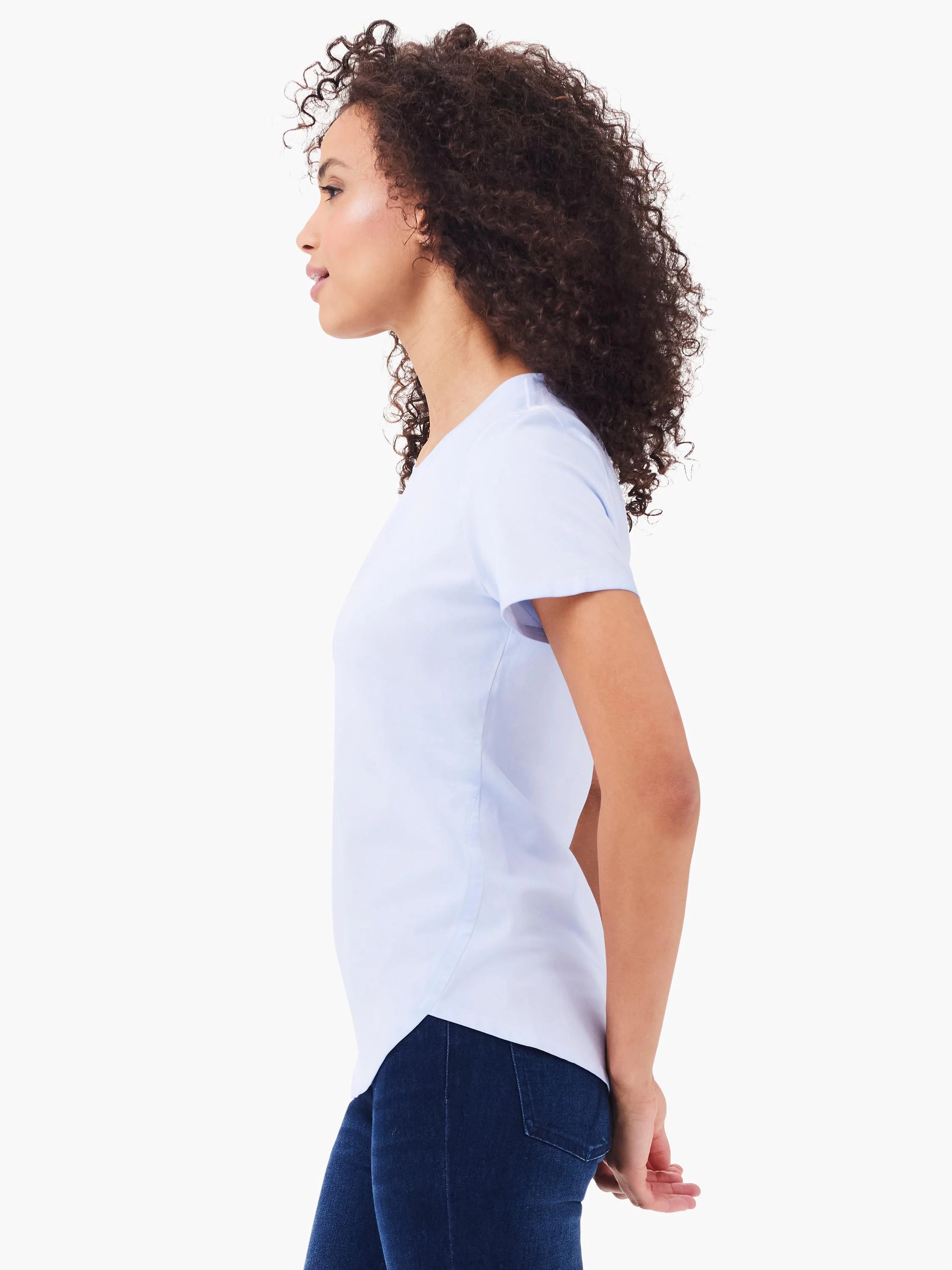 Woman in light blue short-sleeve crew neck tee with shirt tail hem and dark jeans, shown in profile.