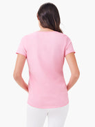 Back view: pink short sleeve shirt tail crew neck tee on a model, worn with white pants.