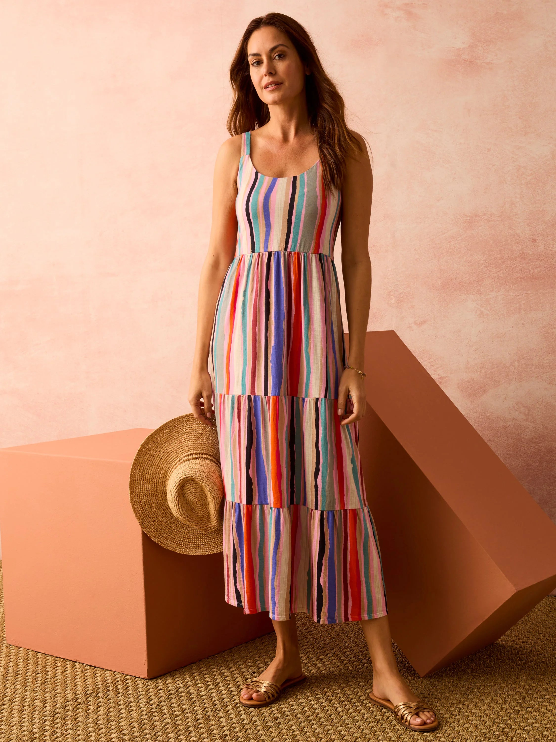 Multicolored vertical stripes on a tiered maxi dress. Off-white background. Pink, red, blue, and teal stripes. Sleeveless.