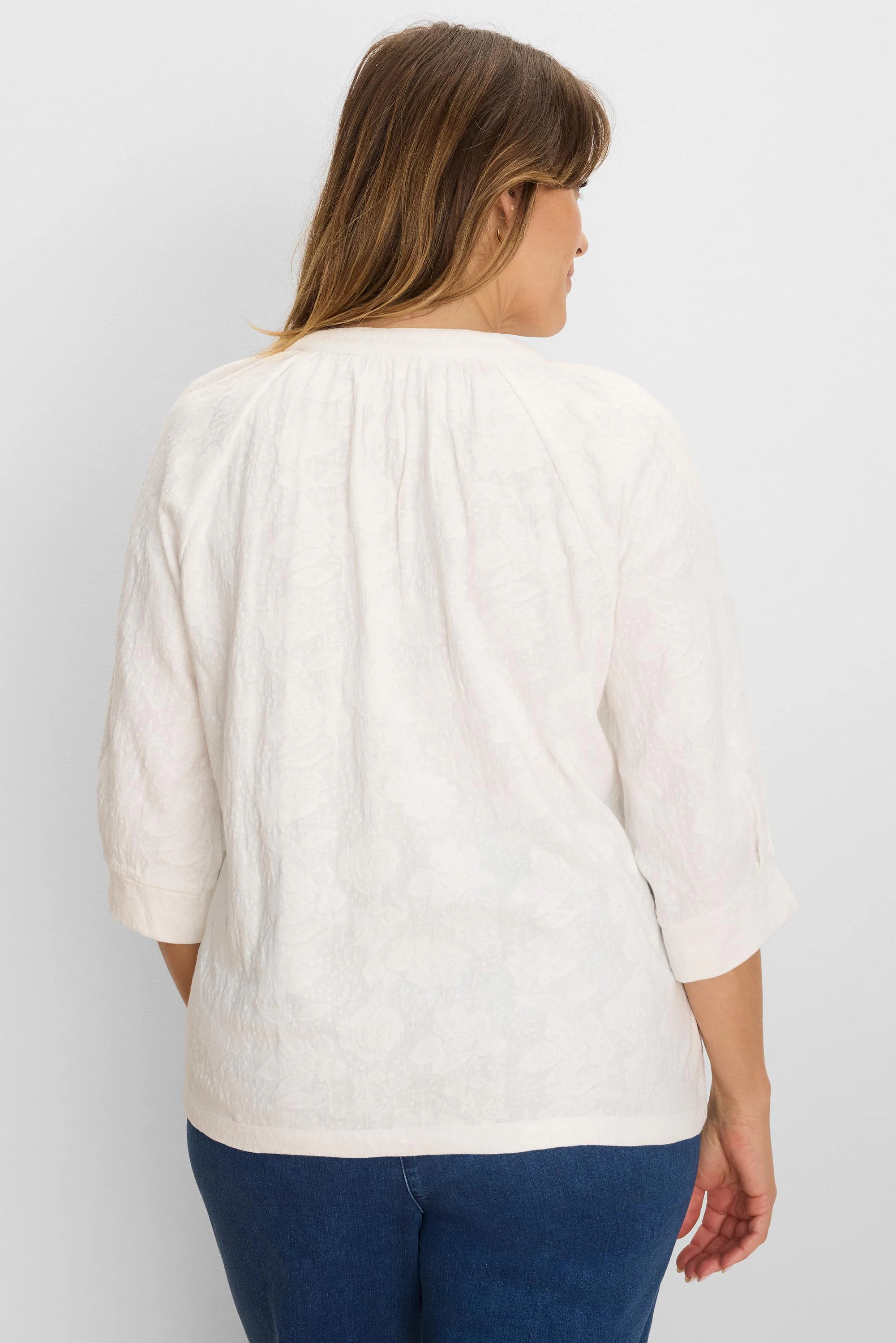 Off-white lace knit top on model, back view. Has 3/4 cuffed sleeves & gathered back neckline.