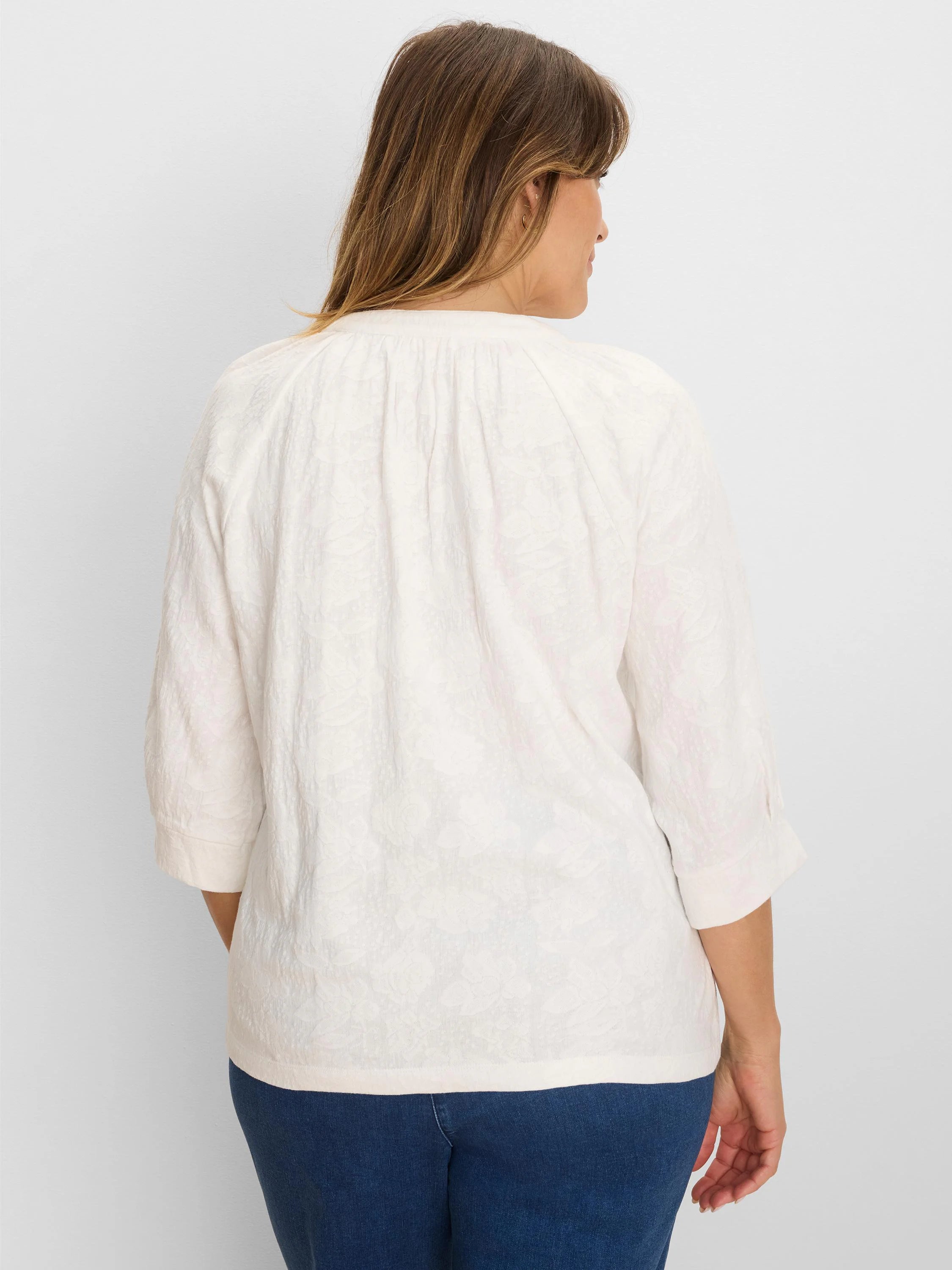 Off-white lace knit top on model, back view. Has 3/4 cuffed sleeves & gathered back neckline.