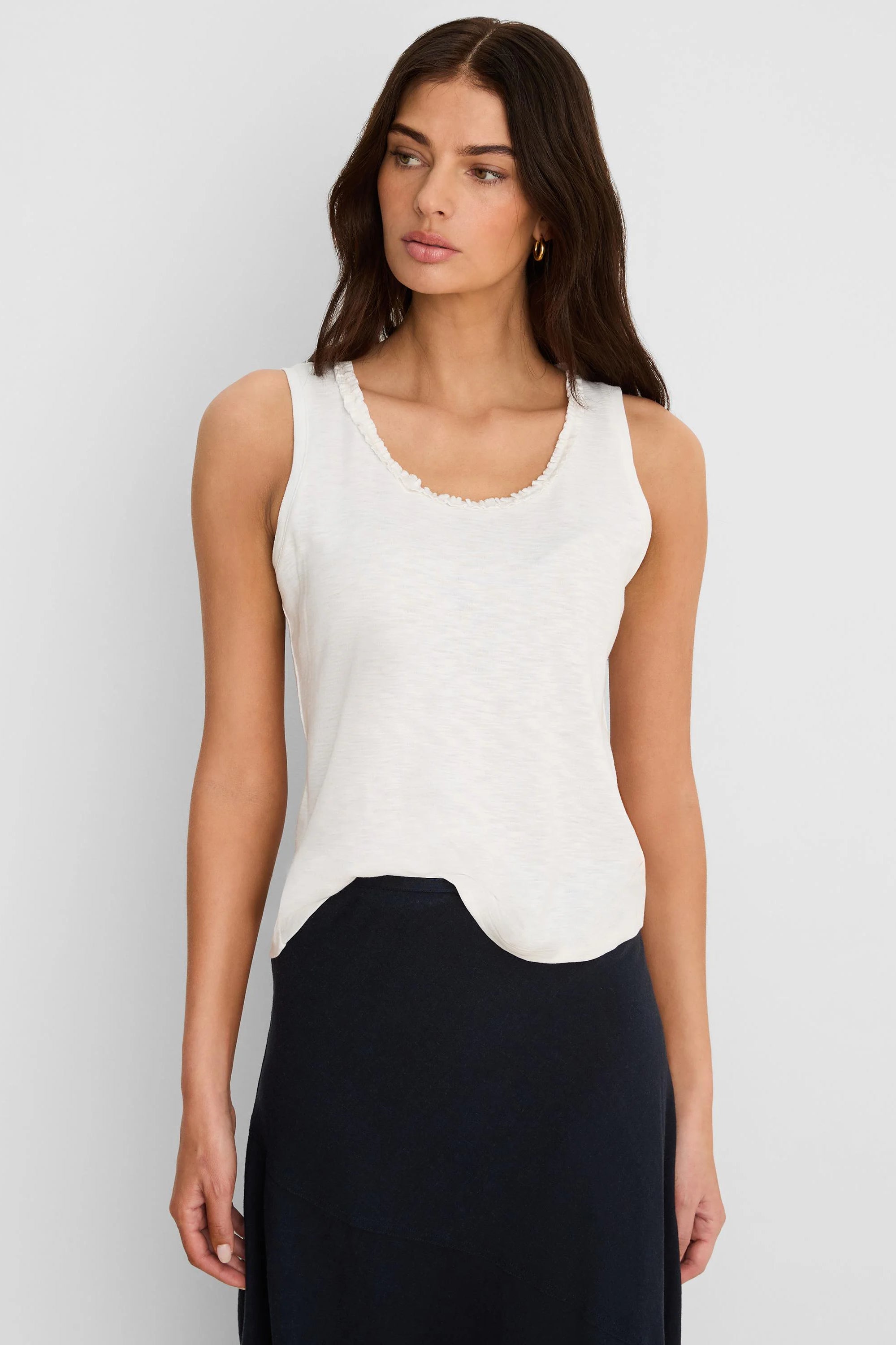 Off-white cotton slub tank top with ruffled neckline and curved hem.