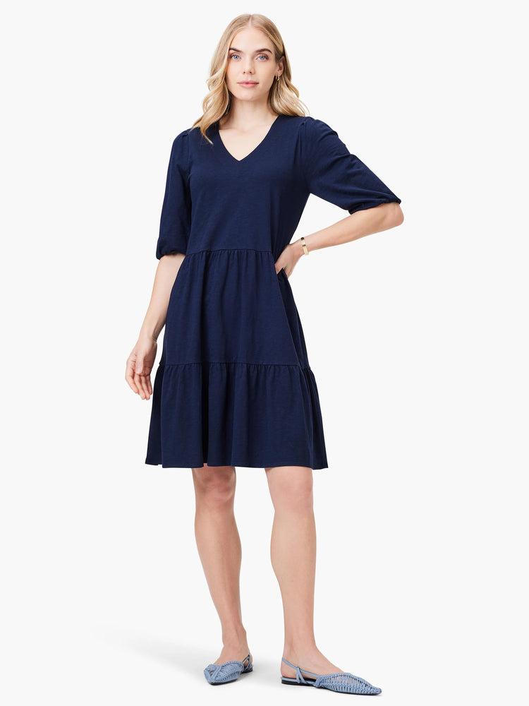 Navy blue tiered V-neck mini dress, elbow-length sleeves. Model wears light blue shoes.