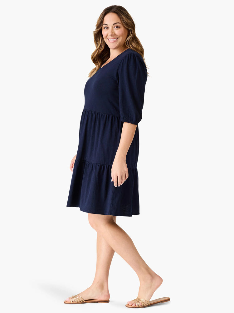 Navy blue tiered V-neck dress with elbow-length sleeves. Model is wearing gold sandals.