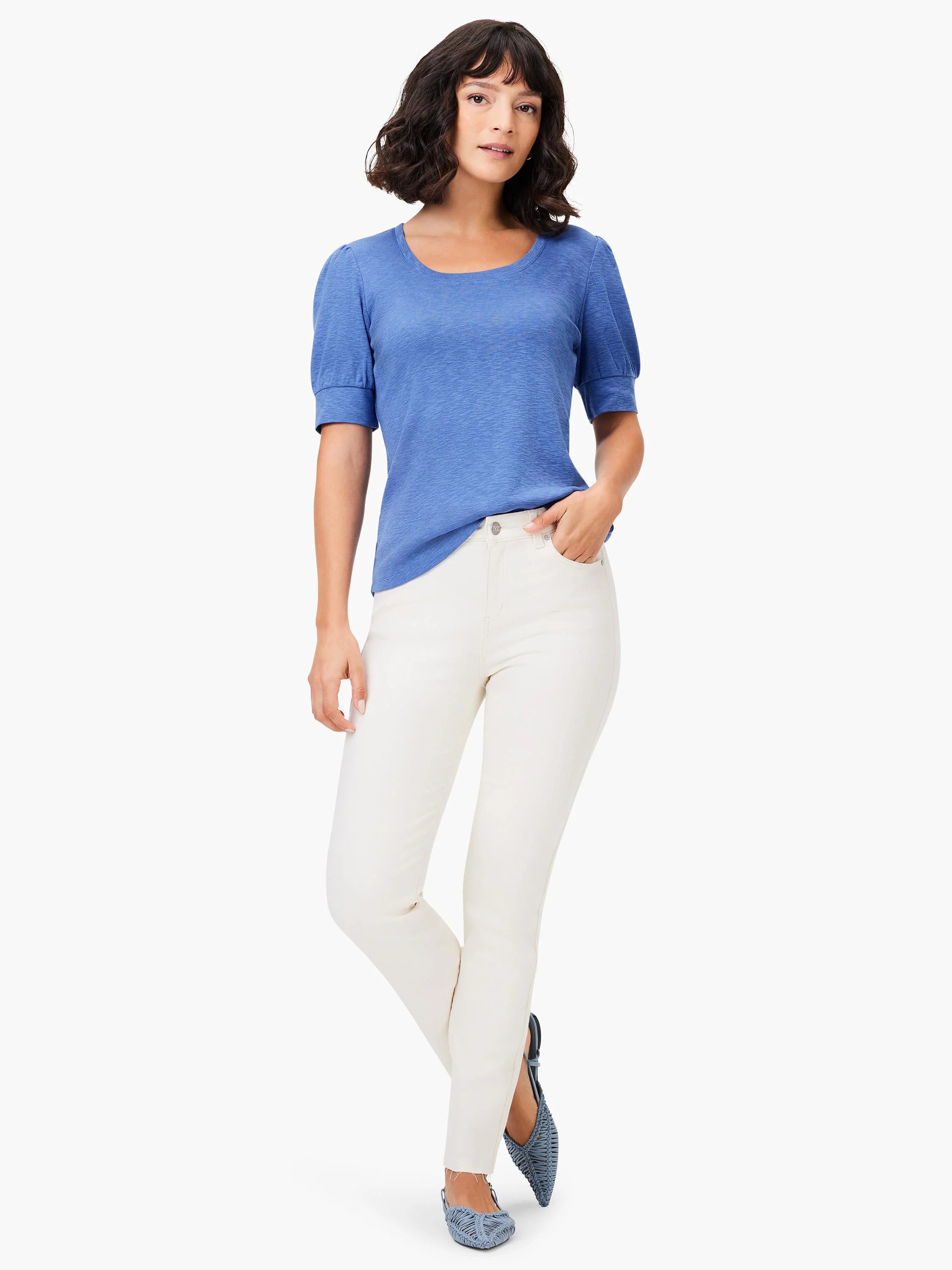Blue scoop-neck tee with short, puffed sleeves. Model also wearing off-white pants and blue shoes.