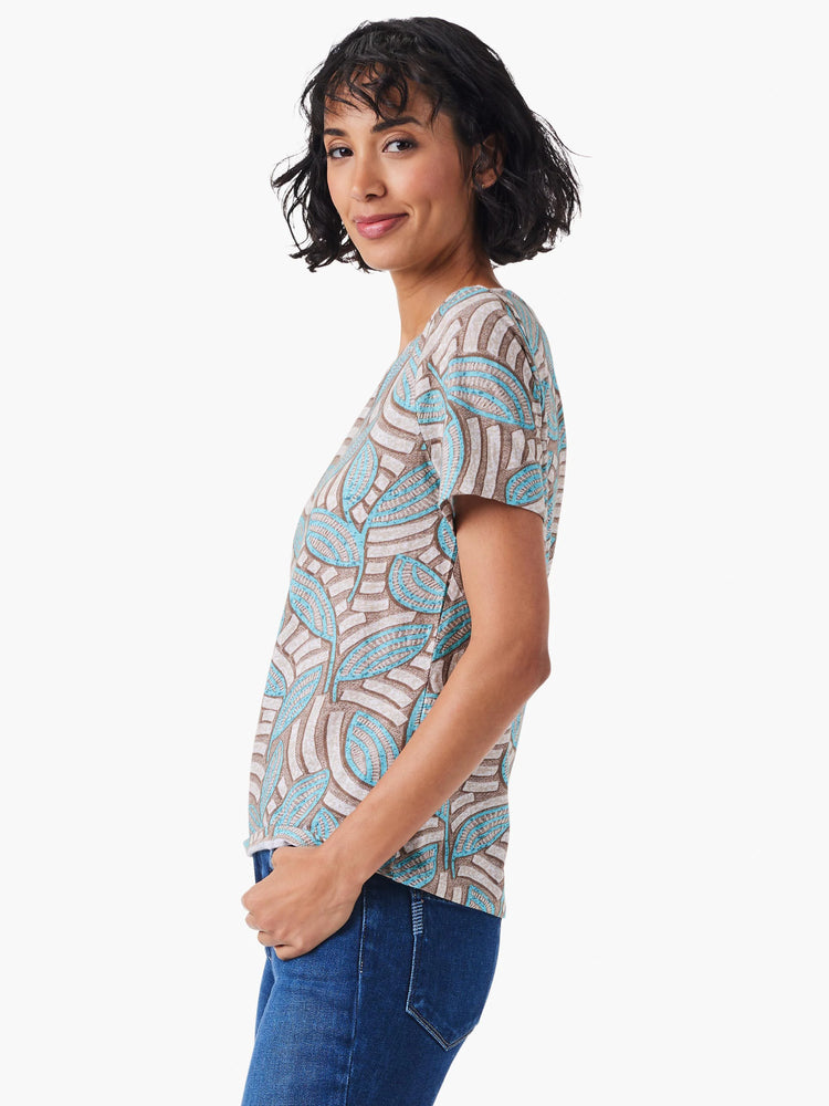 Short-sleeved crew neck tee. Off-white background with teal and brown leaf pattern.