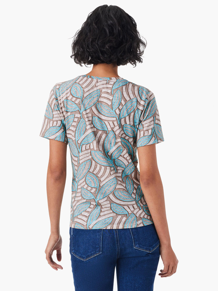 Short-sleeve crew neck tee. Beige background with teal leaf pattern.