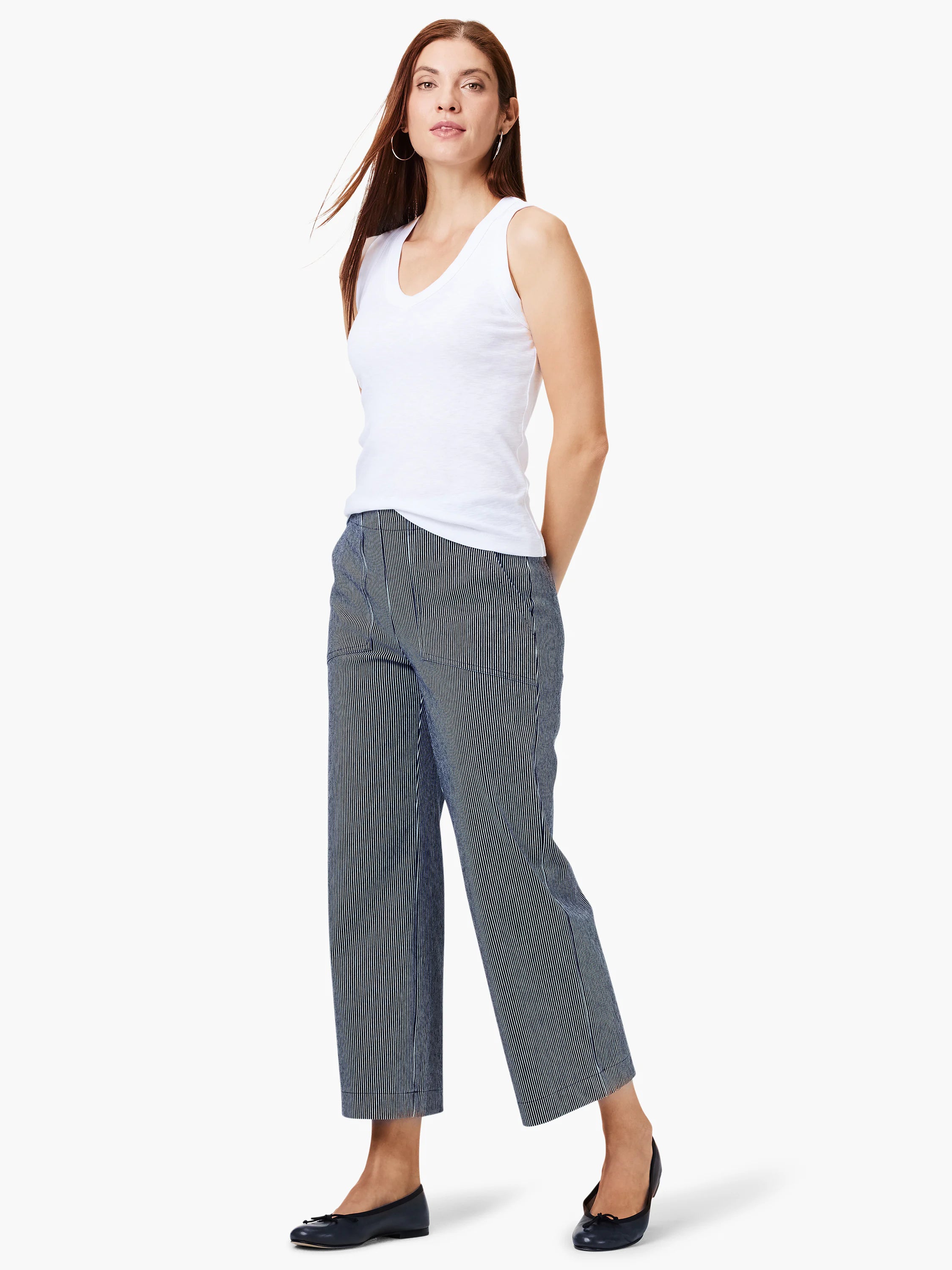 White V-neck sleeveless top; model also wears dark-wash, thin, vertical-striped pants and black flats.