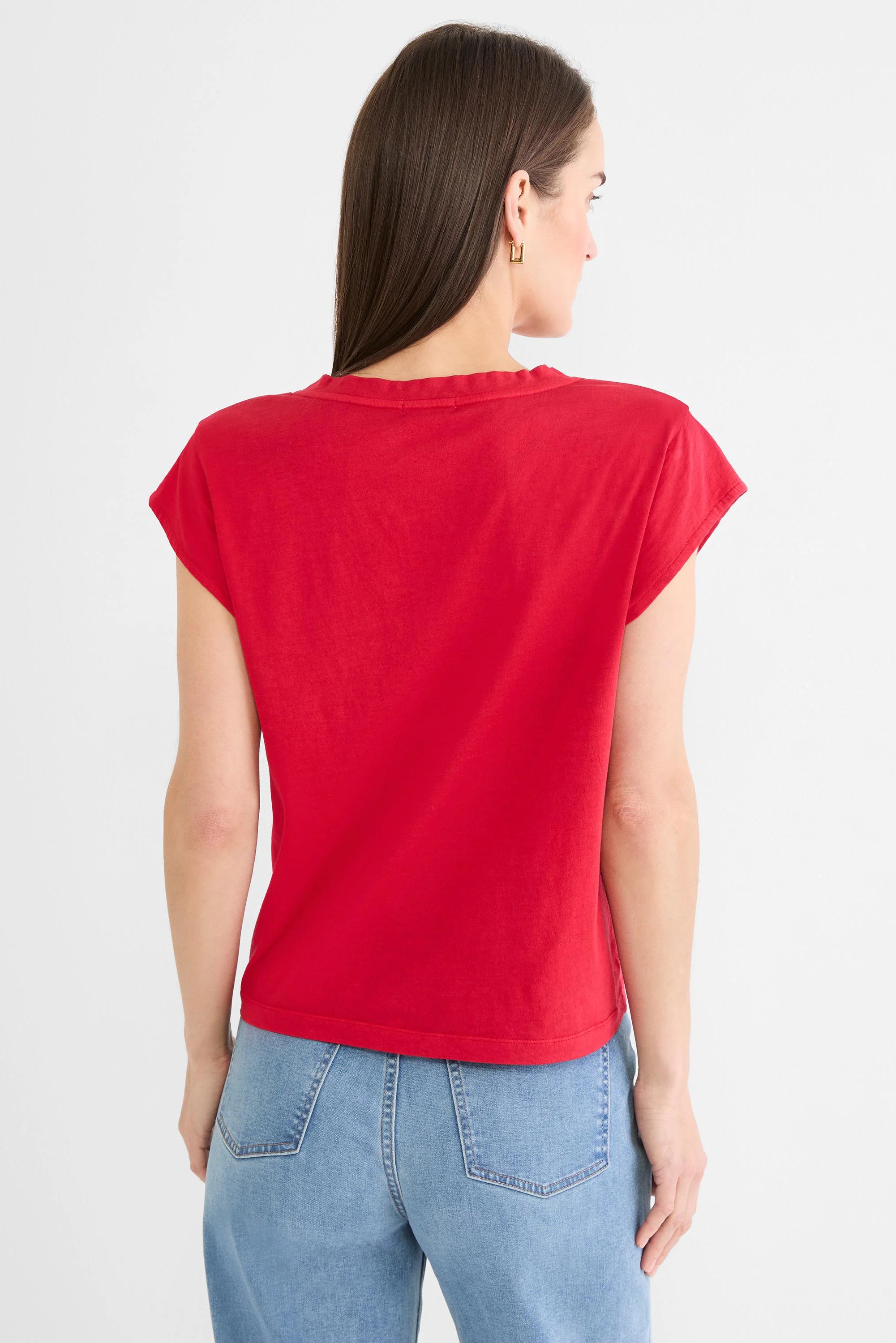 Back view of a model wearing a red cap sleeve tee with a relaxed fit and rounded back neck. Worn with light jeans.