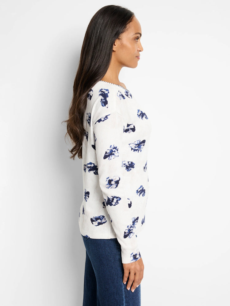 Off-white waffle-knit long-sleeve shirt with a scattered blue floral pattern. Slight off-shoulder neckline.