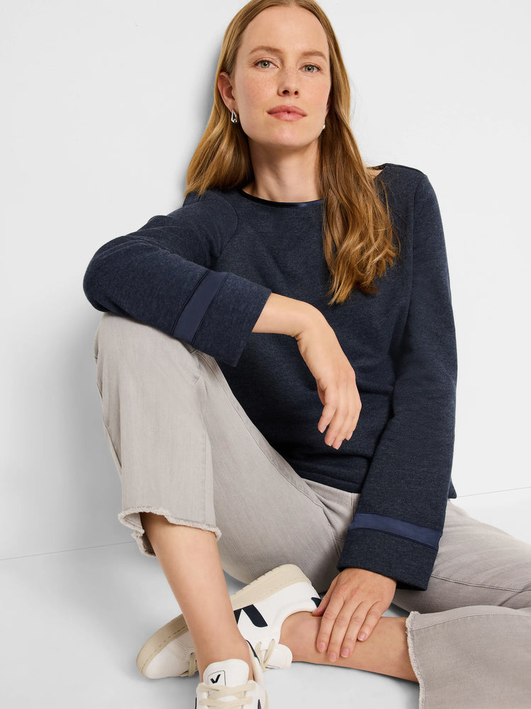 Dark-blue sweater with darker-blue ribbon trim at neckline and cuffs. Model seated wearing light-grey pants.