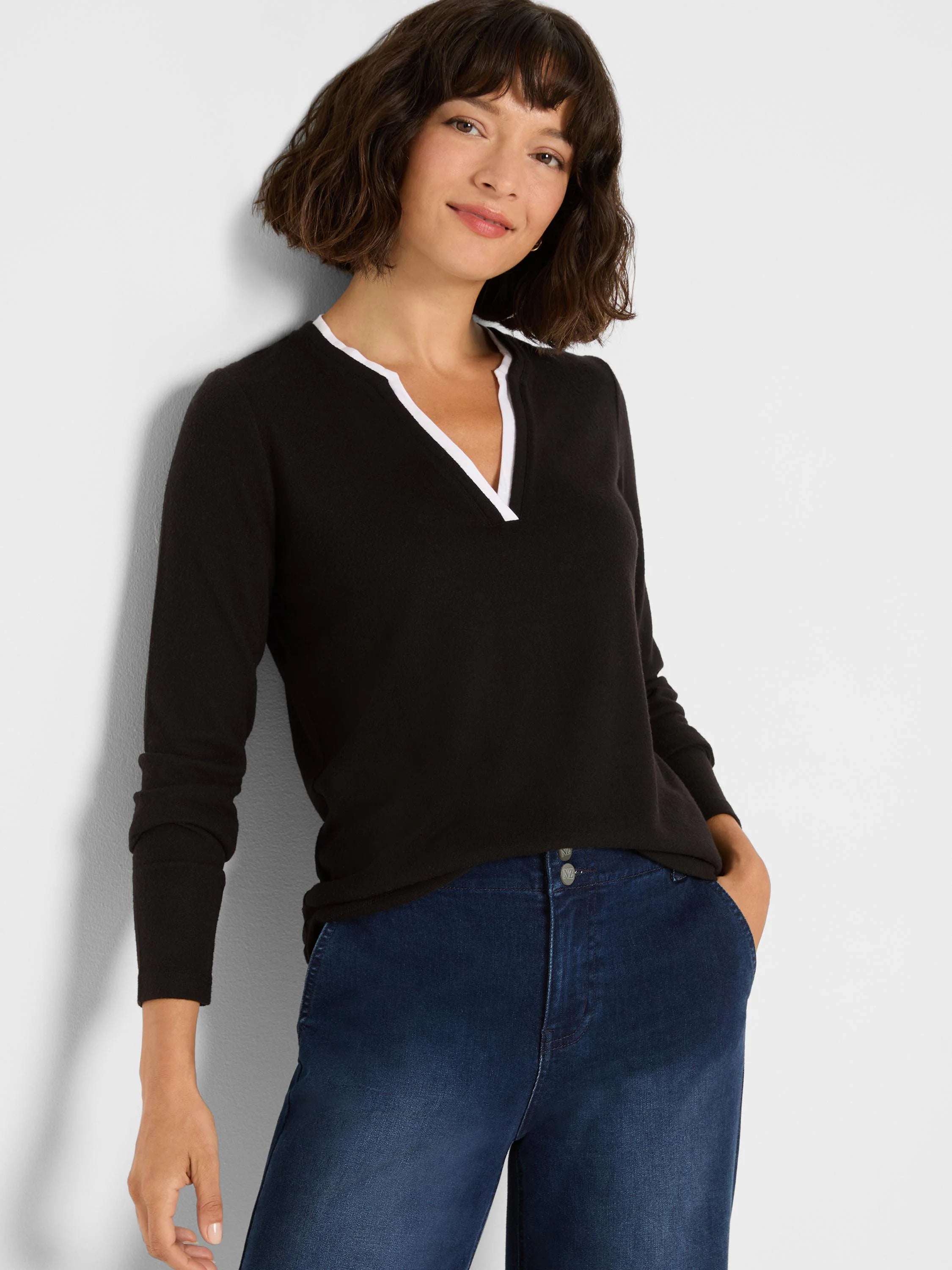 Black long-sleeve top with white-trimmed split V-neck. Model wears dark blue jeans.