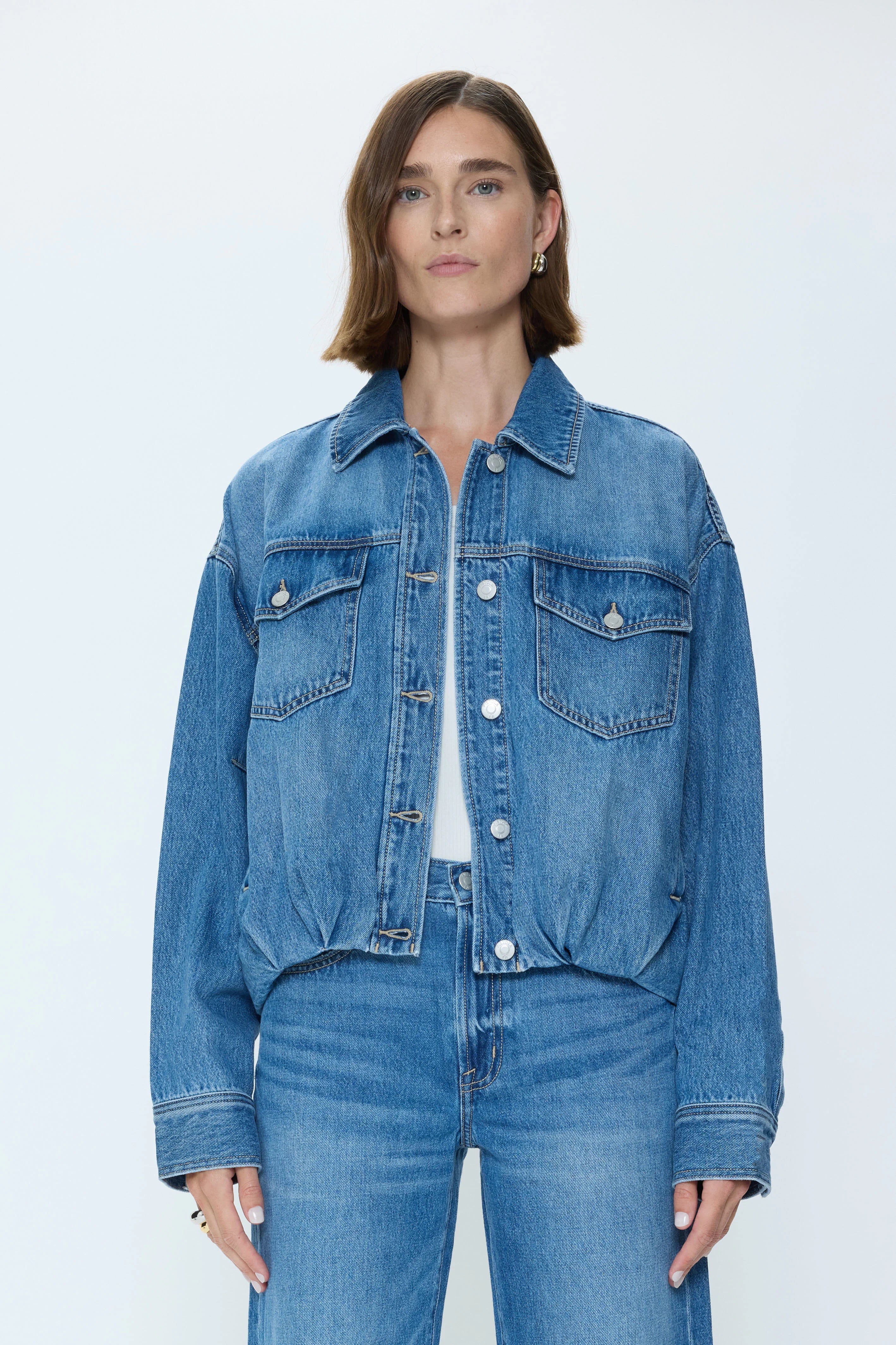 Medium blue denim jacket with cinched blouson hem, collar, silver buttons, and flap chest pockets.