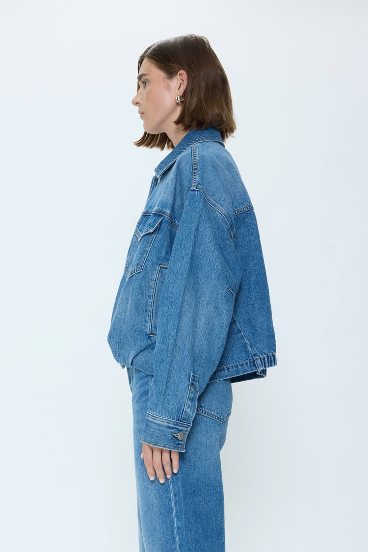 Medium blue denim blouson jacket. Features oversized fit, classic collar, flap chest pockets, and contrast stitching.