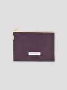 Dark purple cotton pouch with gold zipper and a white "LES PENSIONNAIRES" label on front.