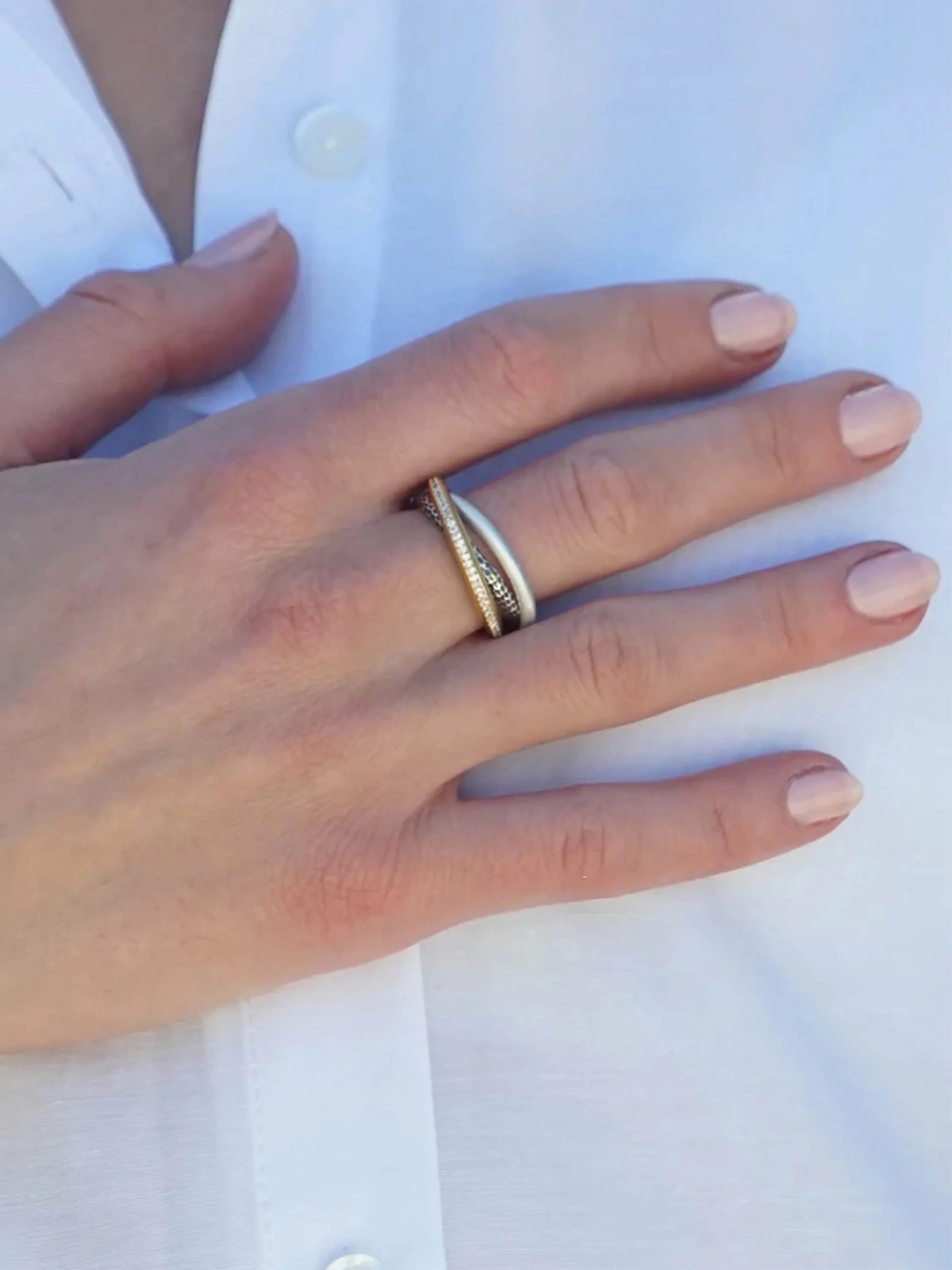 Mixed metal trinity ring with smooth silver, gold pavé, and dark textured bands on a hand.