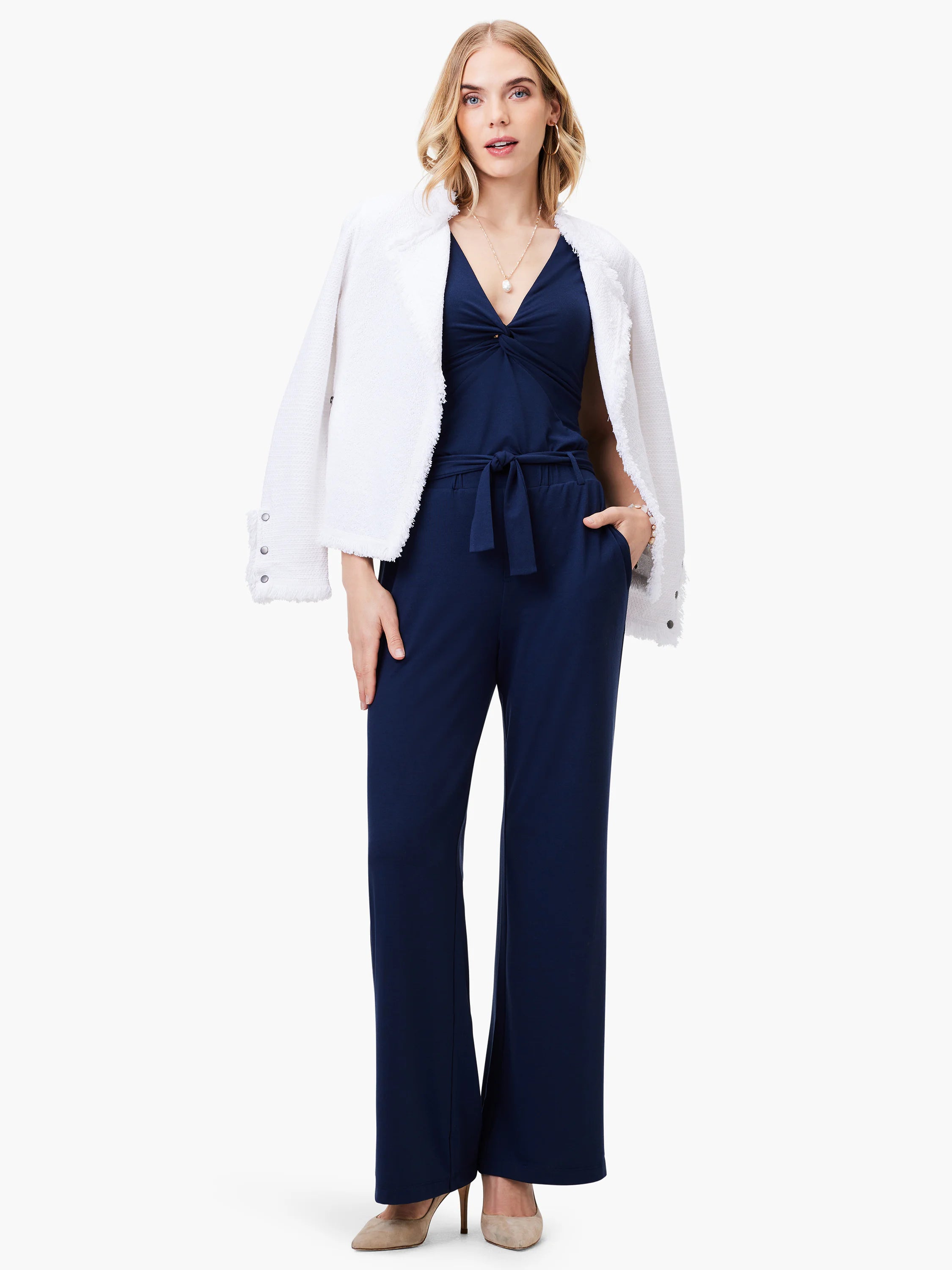 Navy blue wide-leg jumpsuit with twisted neckline; belted waist. Model wears off-white jacket.
