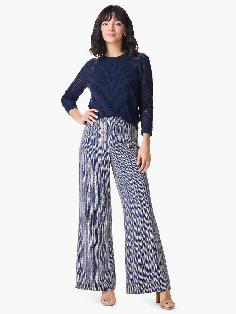 Navy blue pointelle sweater with a geometric pattern. Model also wears wide-leg pants with a vertical navy and off-white...