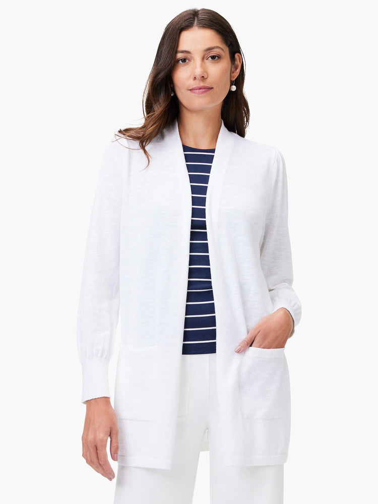 White open cardigan, long sleeves, patch pockets. Model wears it over a navy and white striped shirt.
