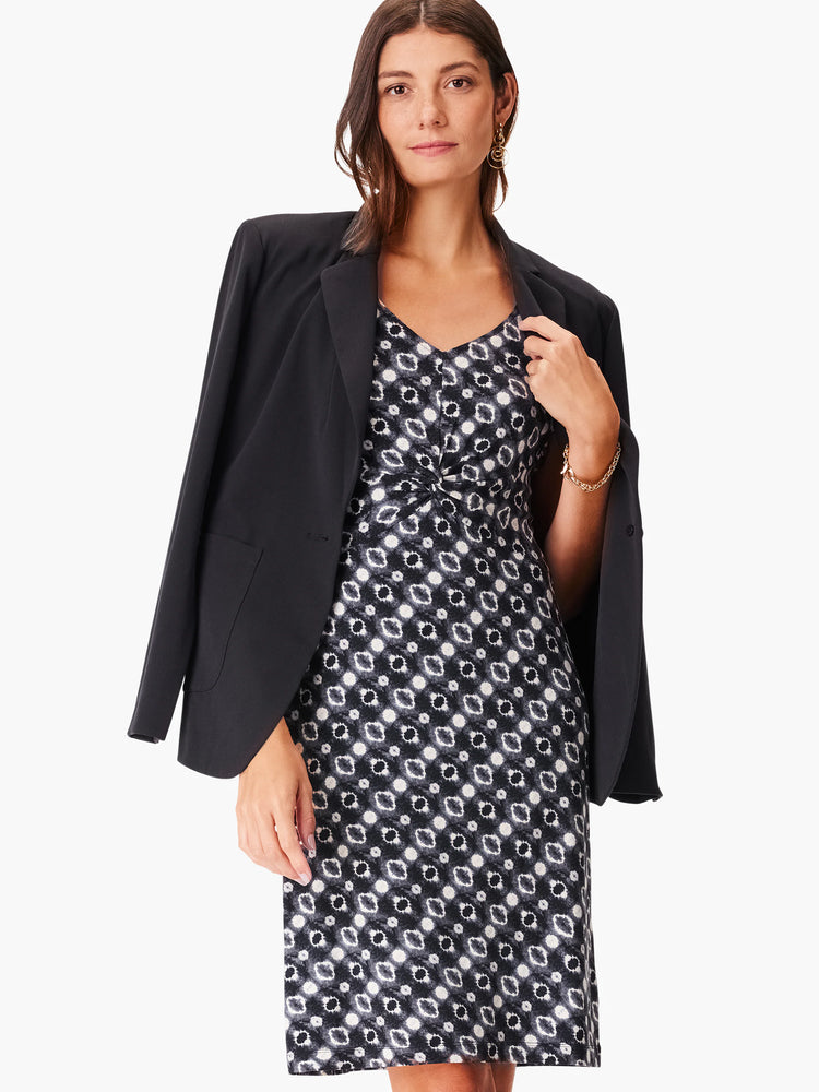 Black dress with a white and gray geometric pattern, V-neck, and a knot detail at the waist. A black blazer is draped...