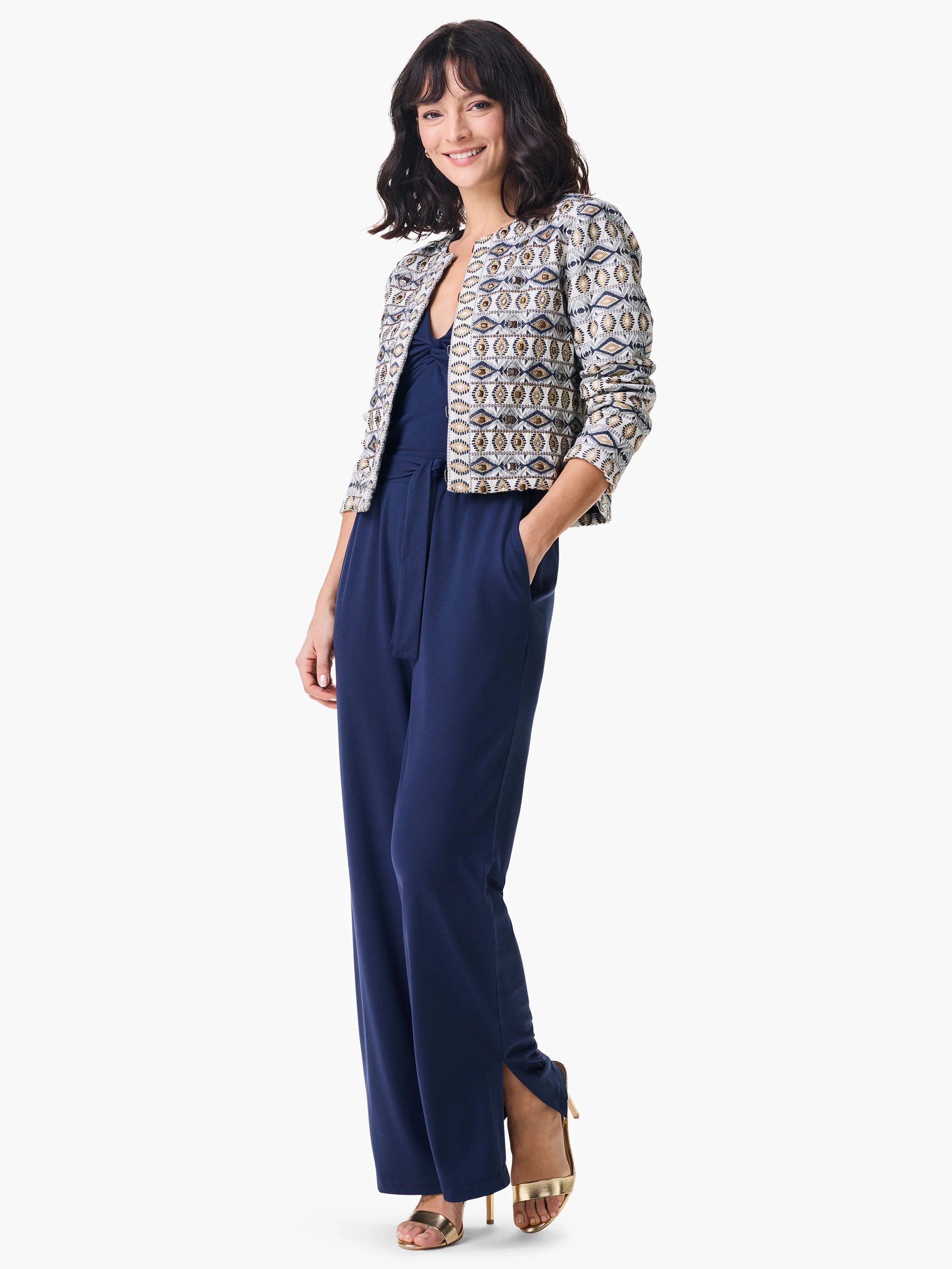 Off-white jacket with navy and gold geometric pattern. Model wears navy jumpsuit and gold heels.