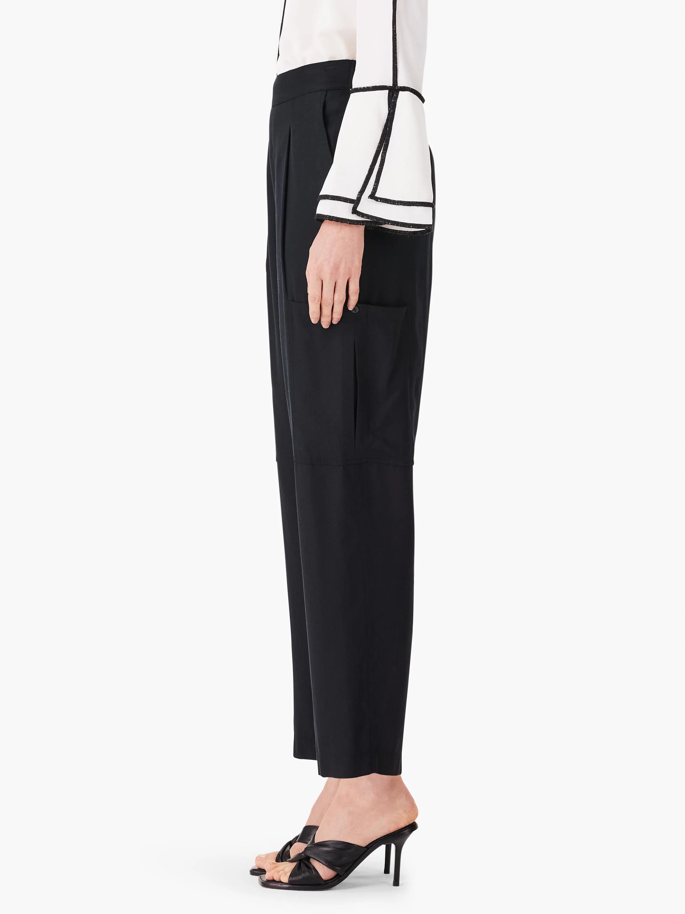 Black cargo pants, cropped, with side pockets. Pleats at waist. Shown on model with off-white top.