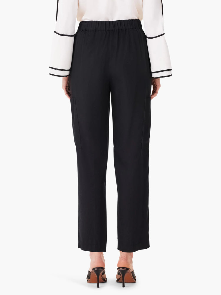 Black cargo pants, relaxed fit, with pockets. Elastic waistband. Model wears shoes; pants shown from rear.
