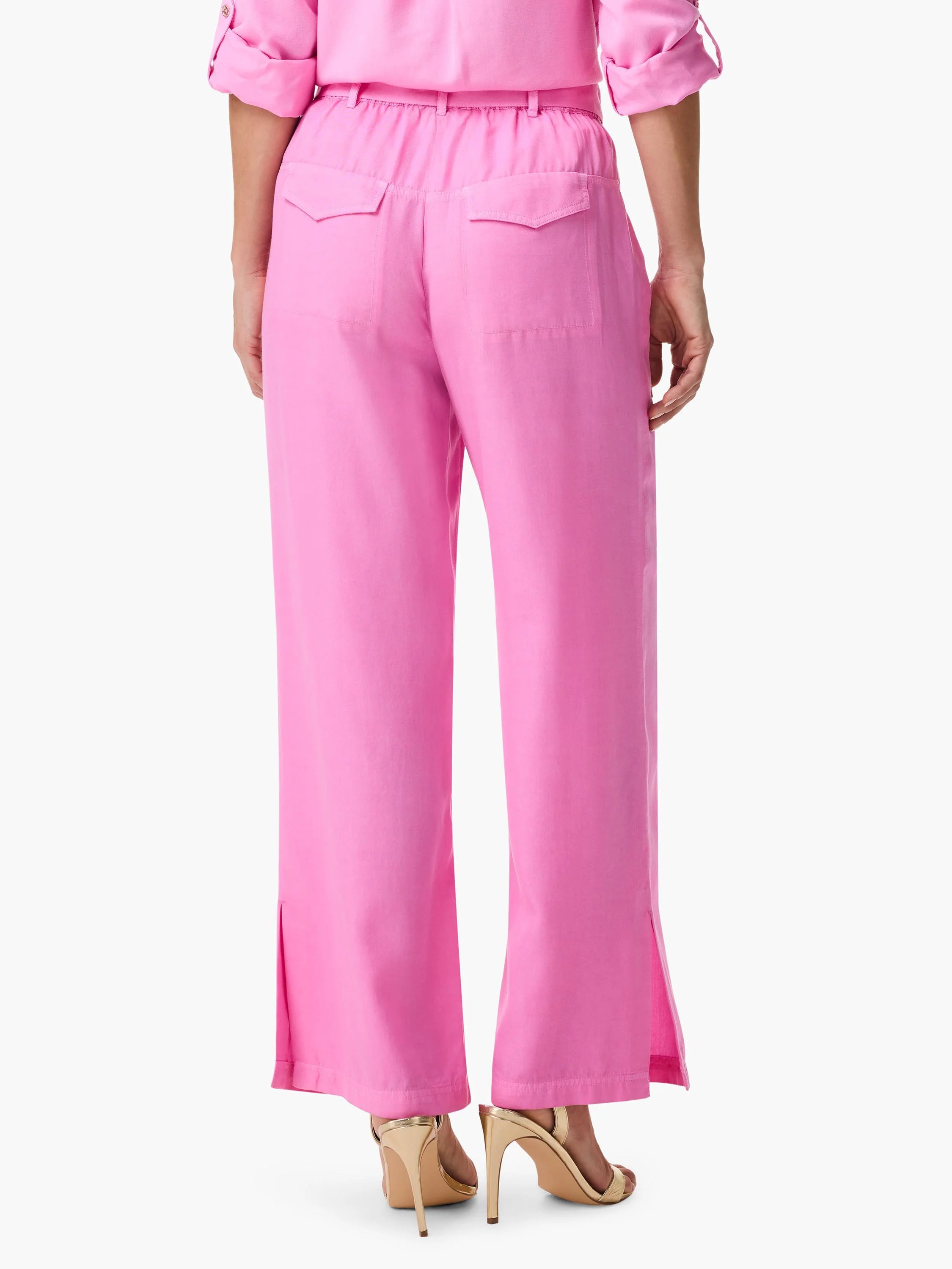 Rear view of drapey pink wide-leg utility pants with gathered waist, back flap pockets, and ankle slits.