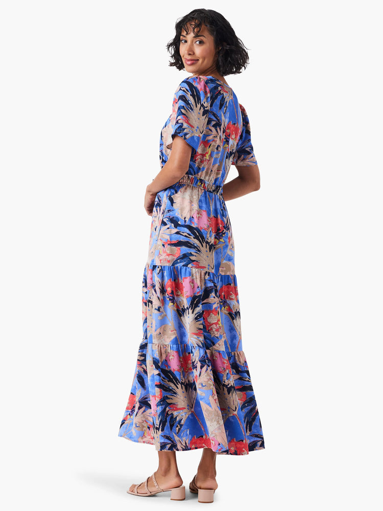 Blue maxi dress with a tiered skirt. Features a pink, red, and beige leaf print. Short sleeves.
