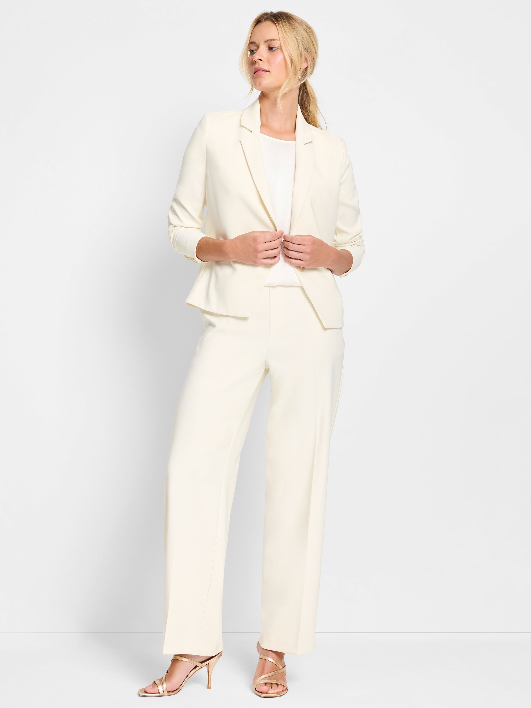 Model wears an off-white tailored suit featuring a fitted blazer and high-waisted wide-leg trousers.