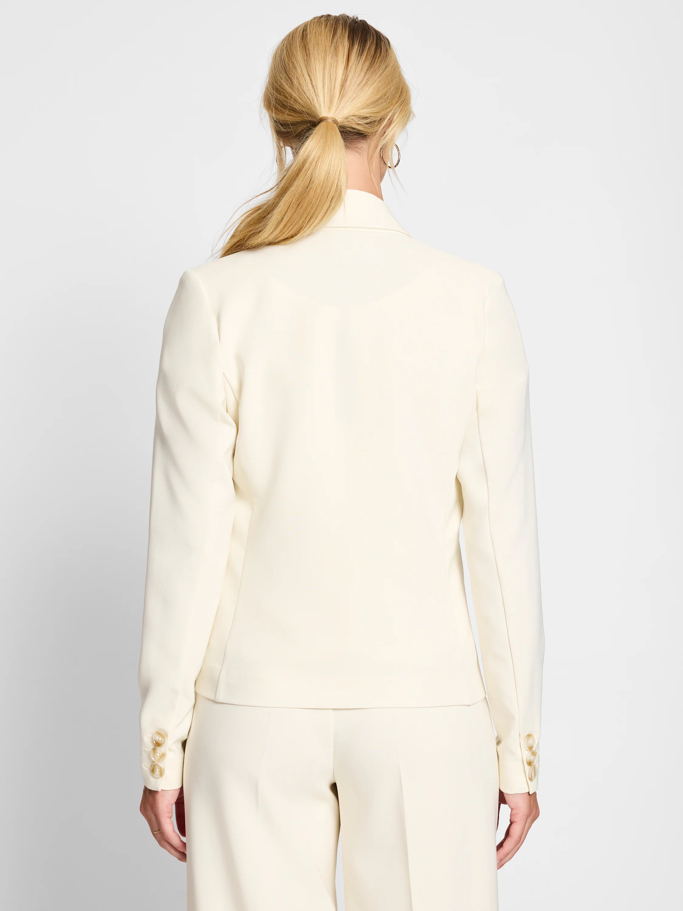 Back view of a cream tailored blazer with three light brown buttons on each cuff.