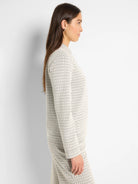 Off-white long-sleeve knit top with a subtle dark V-pattern, creating a textural swirl.
