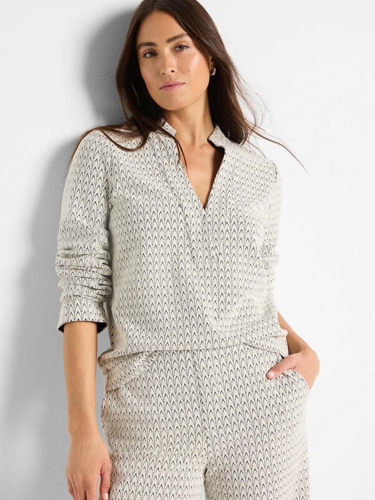 Off-white knit top with dark, subtle swirl pattern, open V-neck collar, and gathered long sleeves.