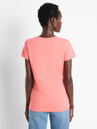 Back view of a coral short-sleeve crew neck t-shirt worn by a model in light blue jeans.