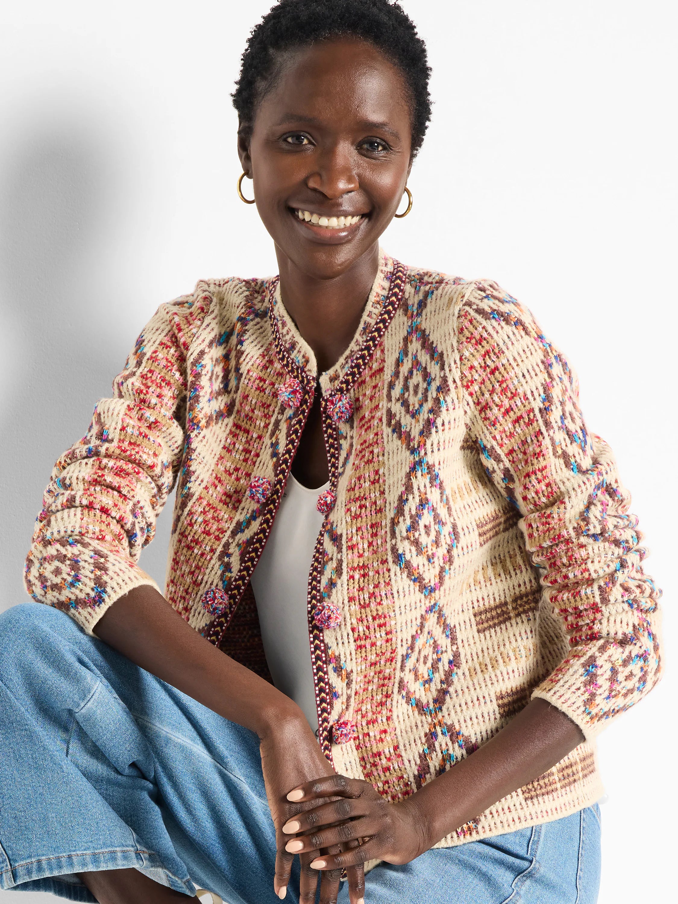 Knit jacket, beige base with multicolored geometric pattern in red, brown, and blue. Pom-pom button details.