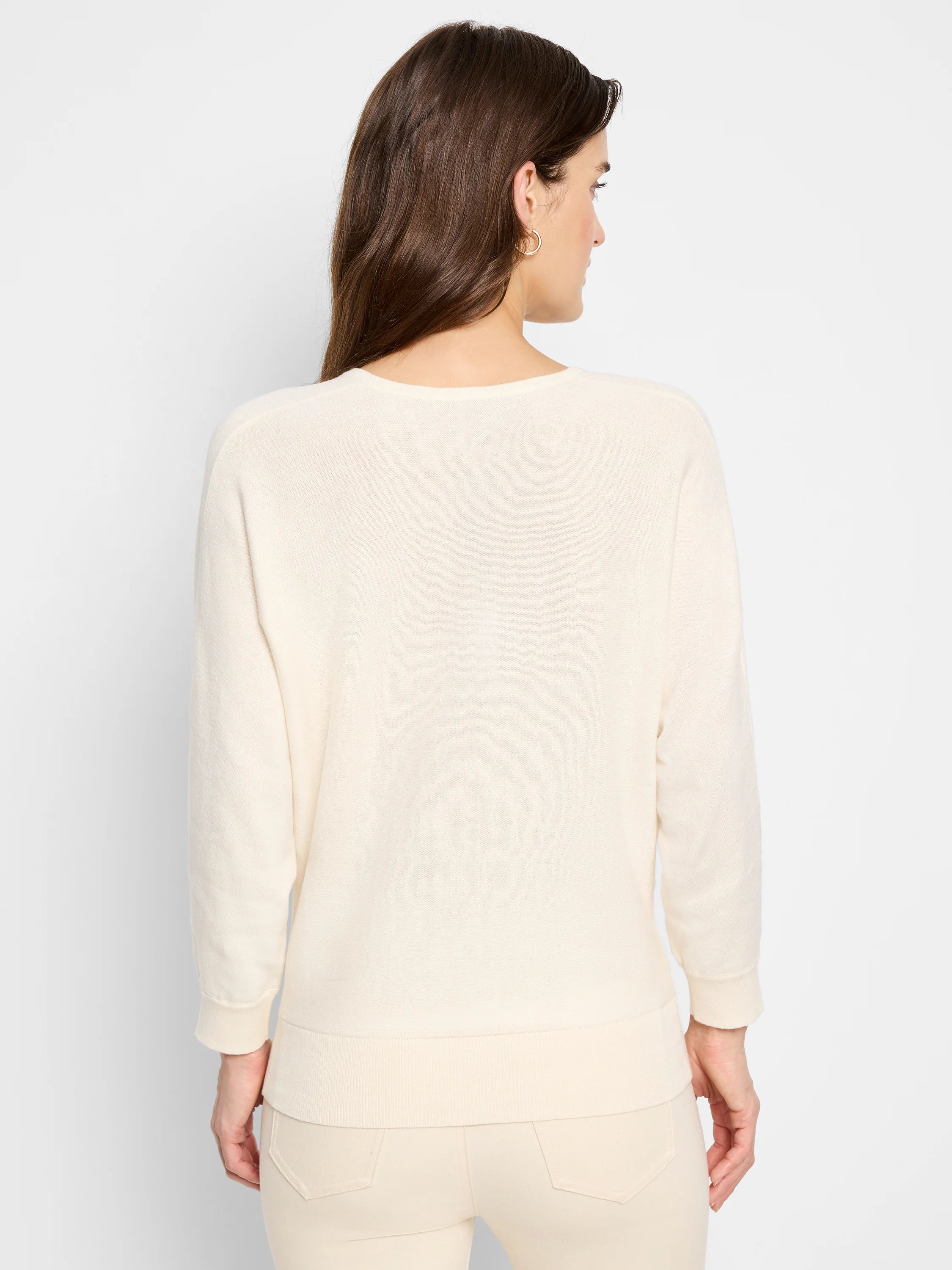 Model from back in a cream, long-sleeved sweater with ribbed cuffs and hem.