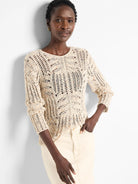Cream open-knit sweater speckled with blue and orange flecks. Loose, textured knit with varied patterns and ribbed cuffs.