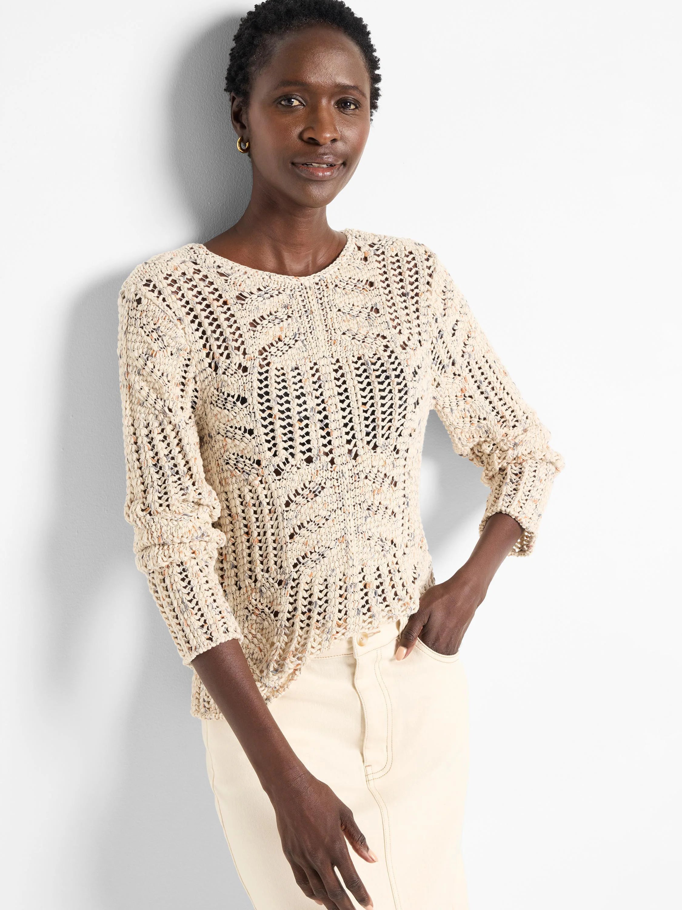 Cream open-knit sweater speckled with blue and orange flecks. Loose, textured knit with varied patterns and ribbed cuffs.