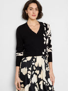 Black sweater with off-white abstract pattern on one side and sleeve cuffs; V-neck with scalloped edge.