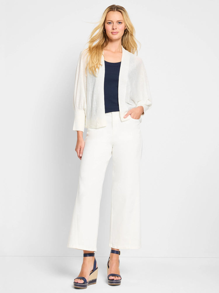 Off-white open cardigan, 3/4 sleeves with fitted cuffs. Model also wears white pants and dark blue shoes.