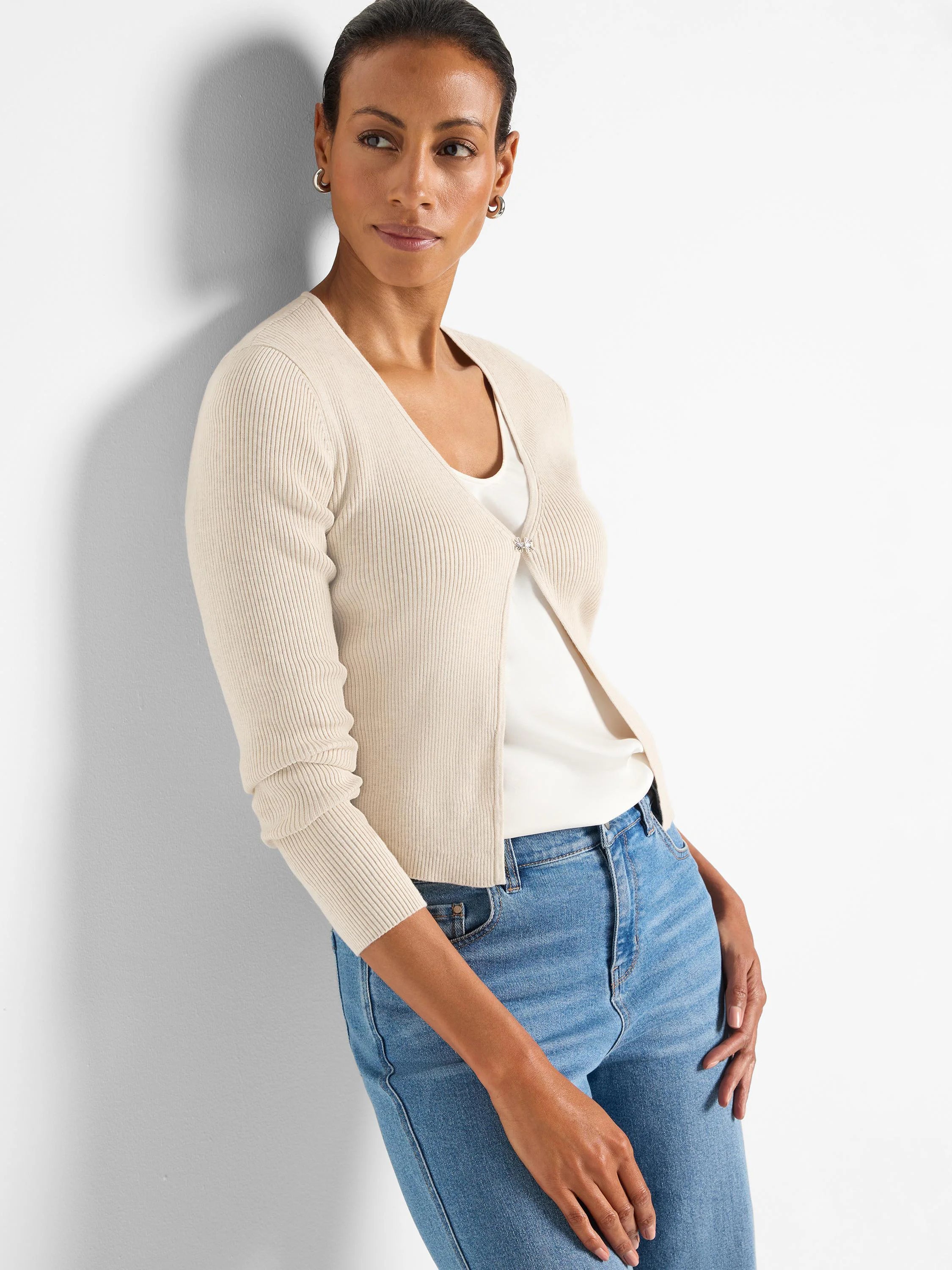 Cream ribbed knit V-neck cardigan with long sleeves and a single silver-toned decorative clasp. Waist-length.