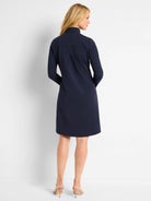 Navy blue, long-sleeved, knee-length knit dress. Mock neck, A-line silhouette.  Back view.