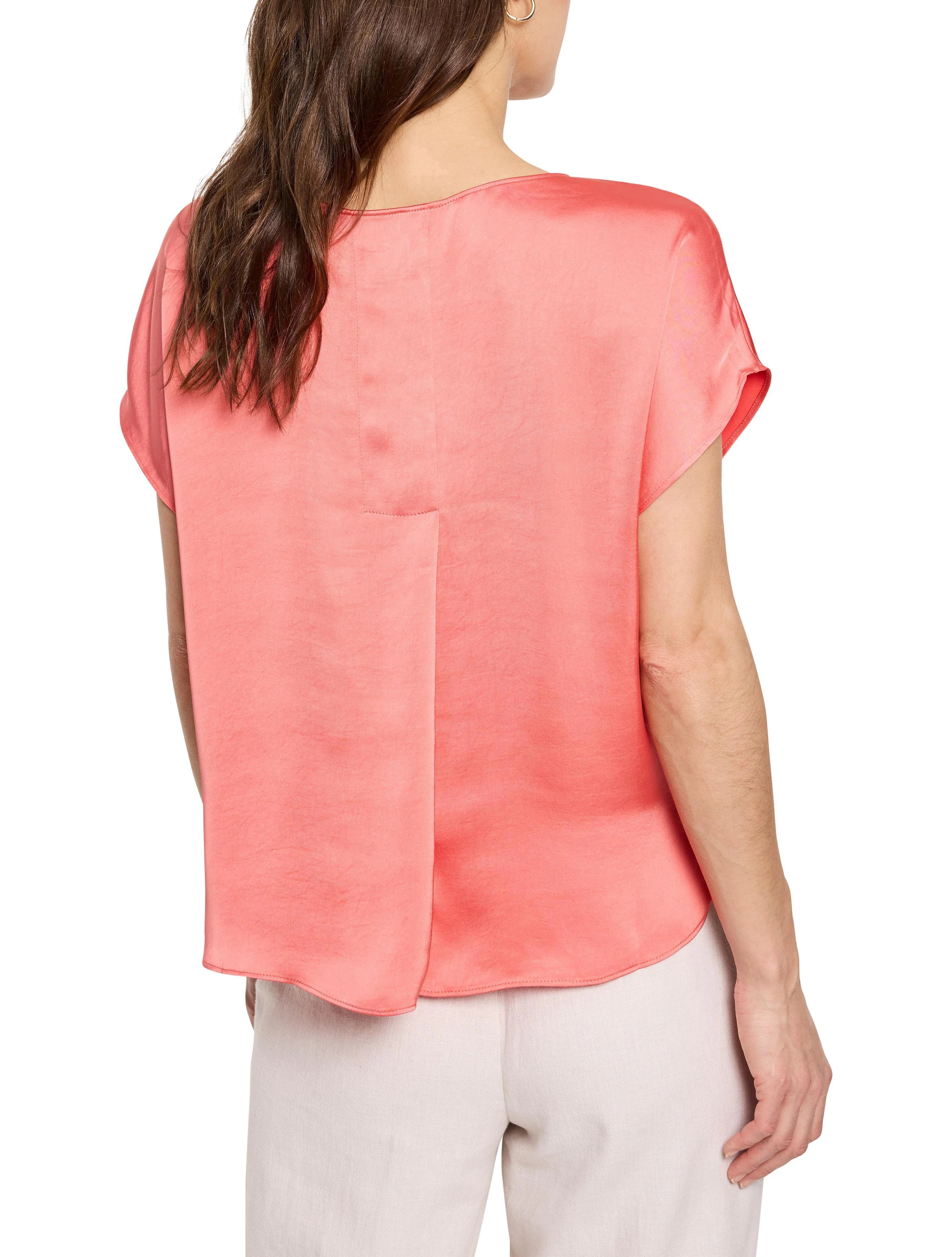 Back view: Model in a glossy coral-pink woven tee with short sleeves and vertical back seam detail.