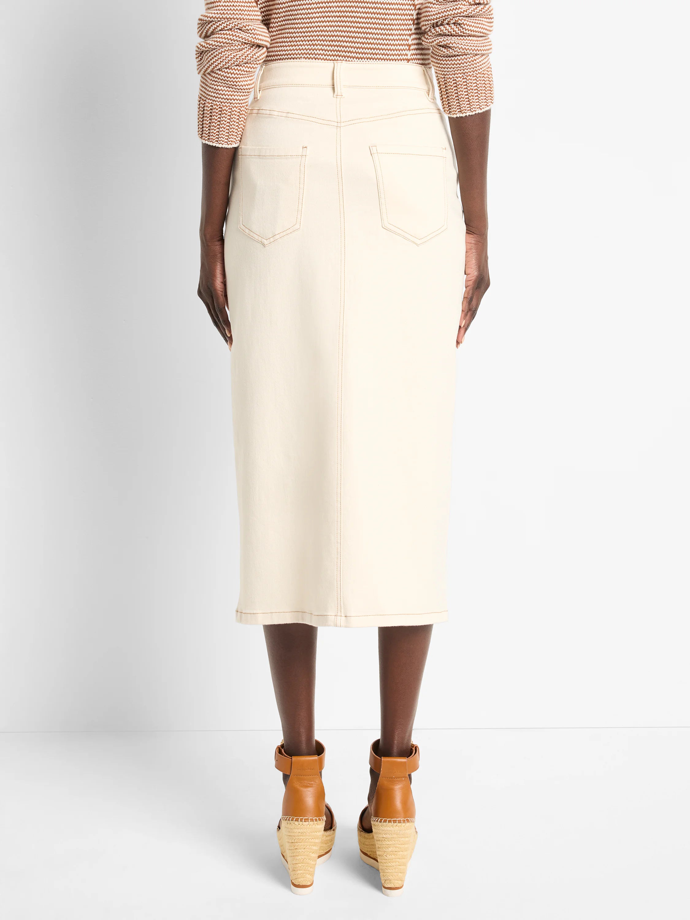 Off-white denim midi skirt with front slit, back pockets, and light brown topstitching.  Rear view.