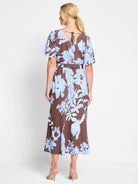 Brown midi dress with light blue floral print, flutter sleeves, and tie back.