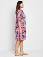 Pink, blue, and peach abstract floral print knee-length shirt dress.  Short sleeves. Model shown wearing gold sandals.