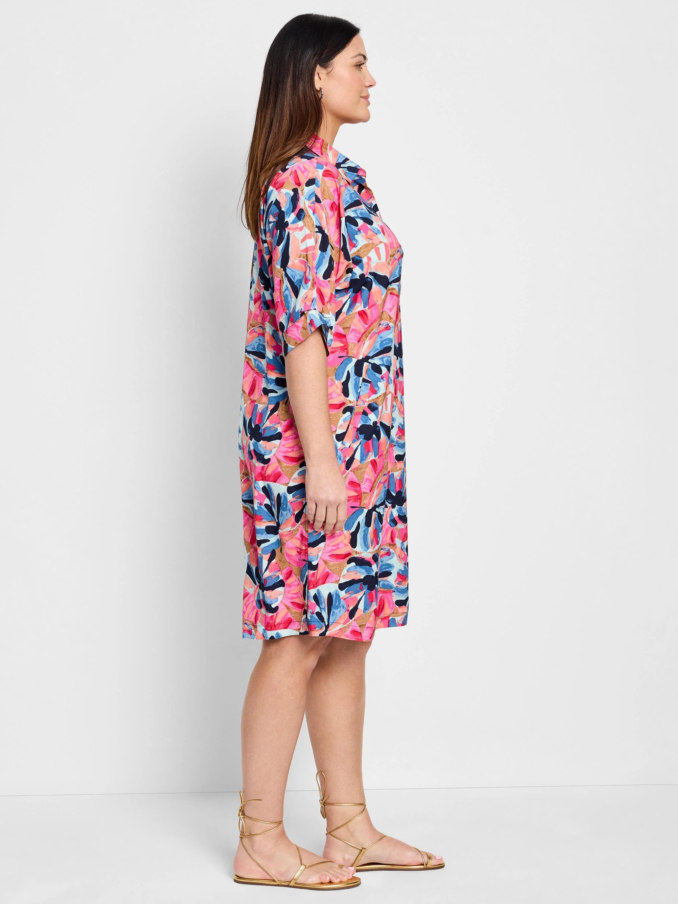Pink, blue, and peach abstract floral print knee-length shirt dress.  Short sleeves. Model shown wearing gold sandals.